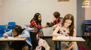 Students in a classroom laughing at image on smartphone.